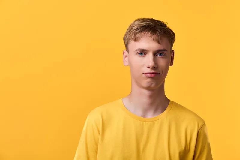 Closeup of a calm young man in casual yellow clothing against a vivid yellow background, minimalist studio lighting, simple composition, warm tone and modern casual appearance