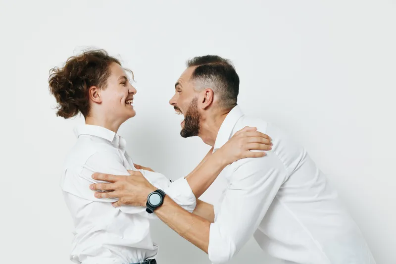 A business professional man and colleague share a warm embrace, set against an isolated colored background, conveying accomplishment, teamwork, and positive emotion in a corporate setting.