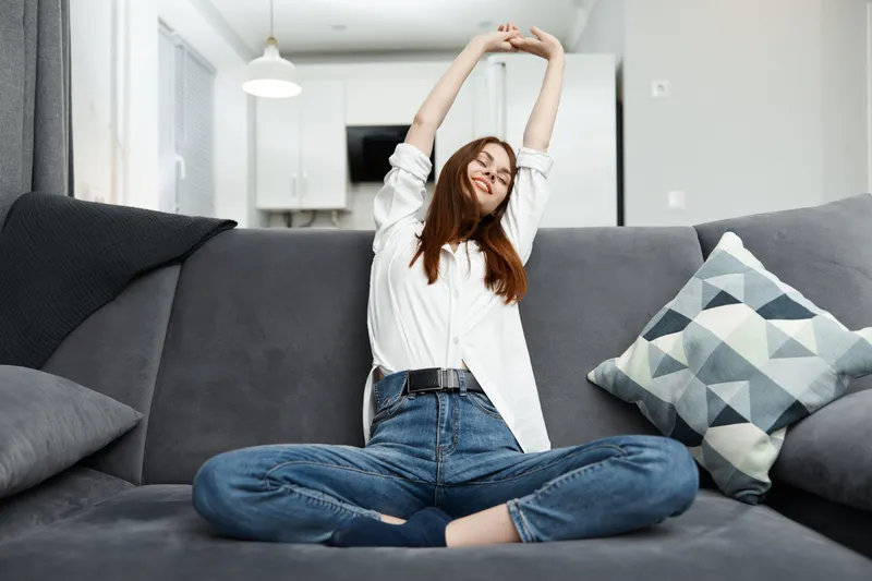 Женщина подтягивается, держа руки над головой, отдыхая на диване дома