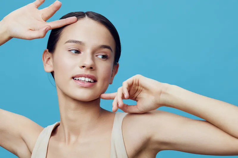A young woman with a joyful expression, posing against a bright blue background, wearing a light tank top, showcasing a trendy, vibrant, and lively concept