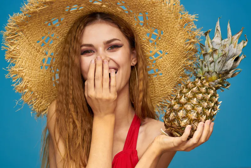 Женщина в соломенной шляпе с ананасом в руках, или это веселье, синий фон, экзотические фрукты