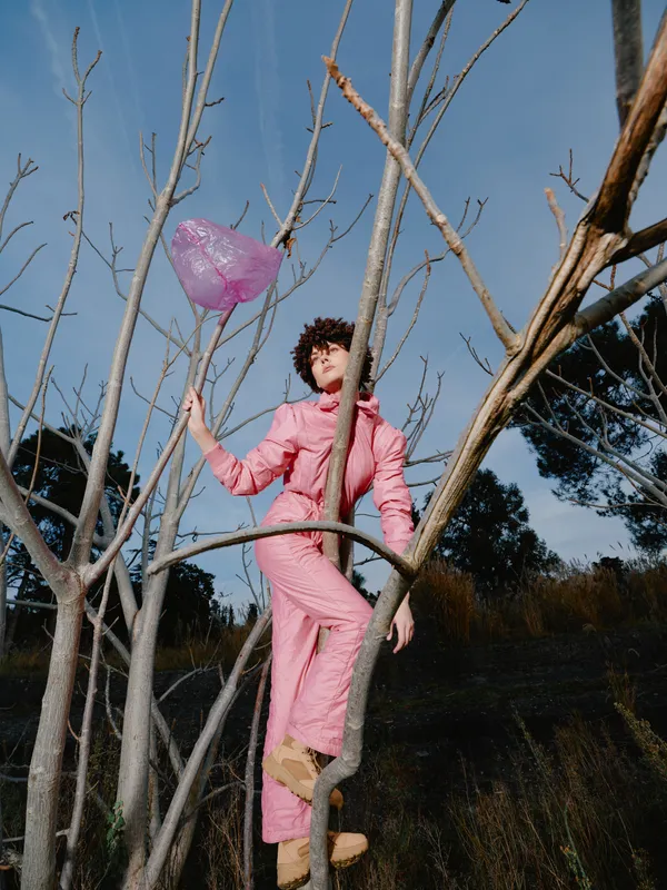 Pink jumpsuit, balloon, tree branches, outdoors, fashion, girl, whimsical, portrait, outdoor shoot, surreal scene with a young woman among bare trees in a colorful meadow, capturing fashion and