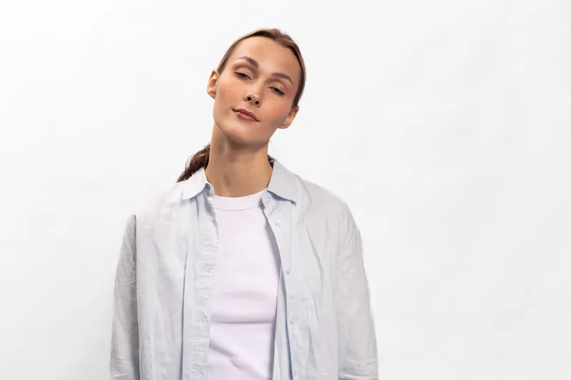 Young woman with closed eyes and relaxed expression stands against white background wearing casual light shirt and white top. Concept for calmness, peace, and mindfulness.