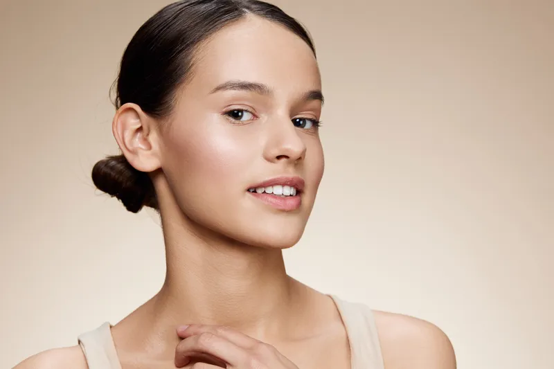 Beautiful young woman with natural makeup and a gentle smile on a neutral background, representing self confidence and beauty in portrait photography