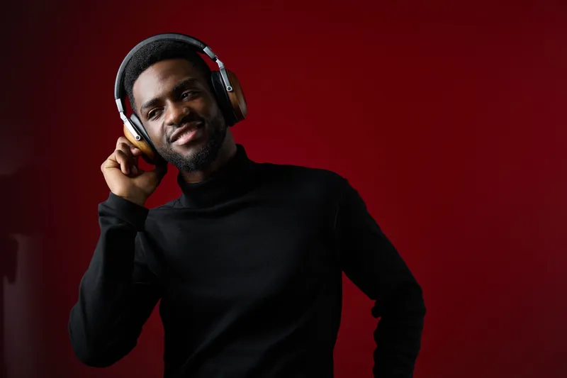 Stylish young Black man enjoying music with headphones against a vibrant red background, exuding confidence and joy in modern fashion