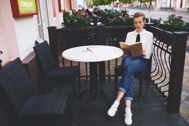 Женщина читает книгу за столиком в кафе
