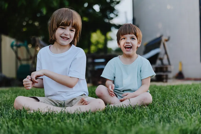 Joyful children playing together on a sunny day, laughing and enjoying time outdoors in a green garden with vibrant grass and warm sunlight.