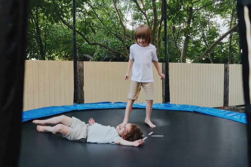 Two joyful boys playing on a trampoline, one standing and the other lying down, capturing the essence of childhood fun and energetic moments.