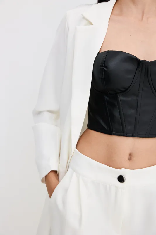 stylish woman wearing a white suit and black corset with a modern minimalistic look, showing part of her torso in a clean, bright studio setting