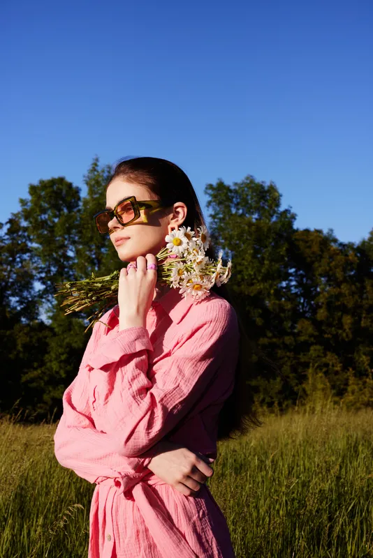 Young woman in a pink dress holding flowers in a sunny field, showcasing serenity and style in a natural setting, ideal for spring and summer themes