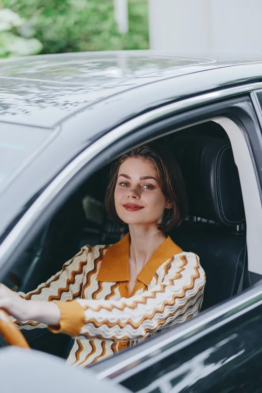 Portrait of a woman driving a car, smiling confidently from the driver's seat, with natural lighting and relaxed mood.