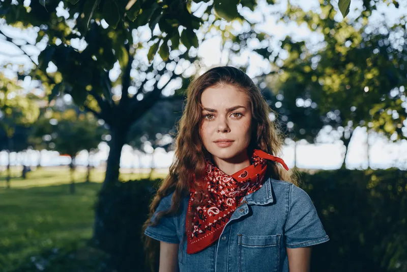 lifestyle woman in modern boho-western denim street style wearing red bandana outdoors with soft film color capturing natural light and relaxed mood