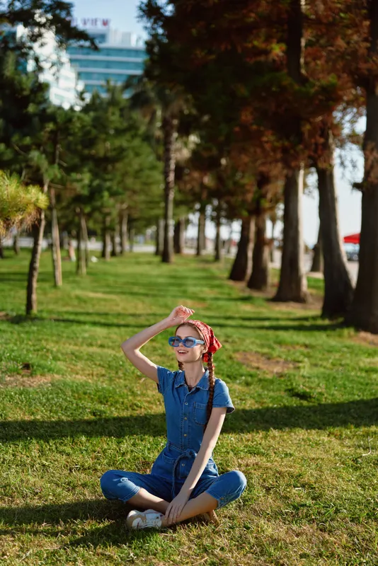 lifestyle woman wearing modern boho-western denim street style sitting cross-legged on green grass in sunny park with film color effect, casual and relaxed mood