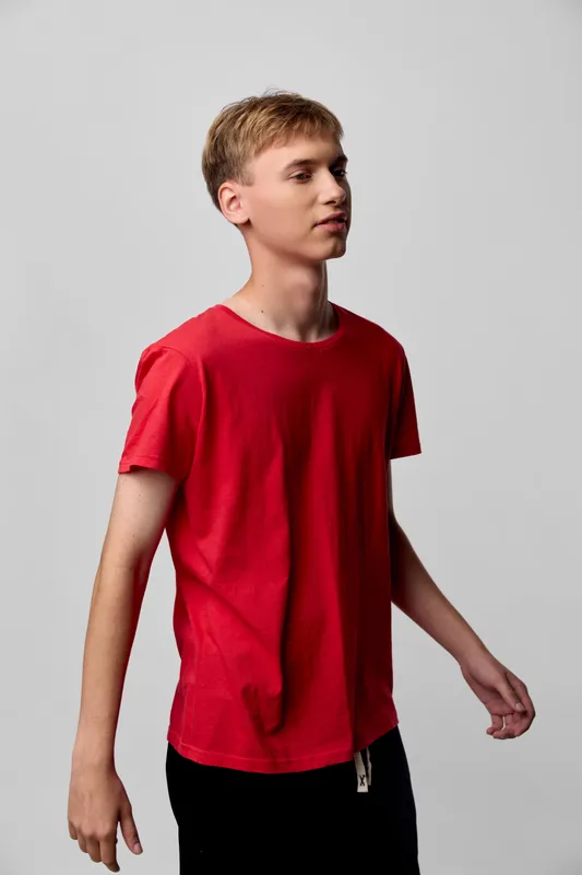 Man in a red shirt stands in a studio shot with a minimalist background, highlighting casual wear, modern fashion, and a lean frame in a relaxed pose for lifestyle and youth styling