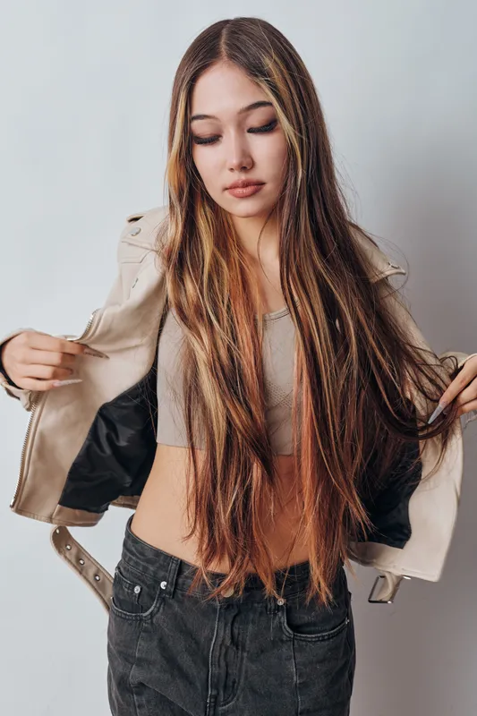 Young woman with long hair wearing crop top and jacket, posing indoors with casual look and natural makeup, isolated on light background.