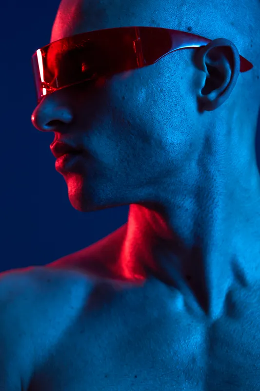 Stylish man with sunglasses striking a pose in an artistic blue and red lighting setup, showcasing a modern, edgy aesthetic and confident vibe.