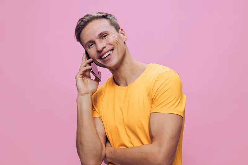 smiling man talking smartphone wearing yellow t-shirt on pink background digital nomad communication concept cheerful lifestyle portrait