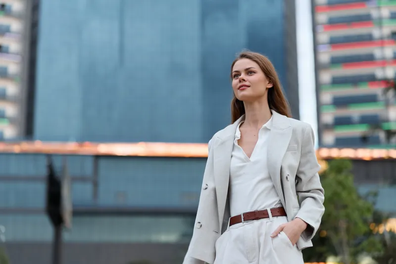 confident business woman in white jacket walking in modern urban environment with skyscraper background