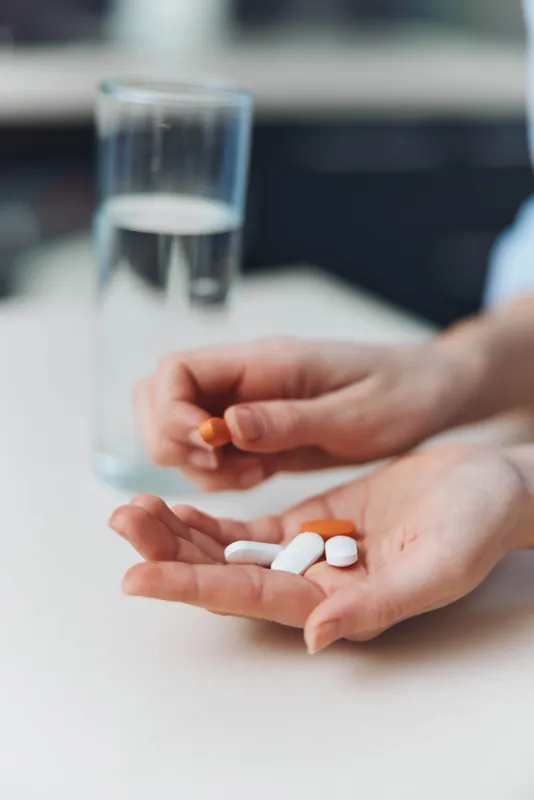 Женщина держит в руках таблетки и стакан воды