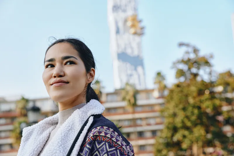 woman outdoor sunlight fashion scarf jacket urban building backdrop expression travel journey street culture scenery lifestyle whimsy style lighting through fabric and texture combining casual