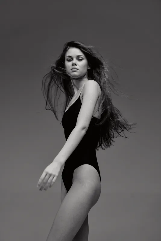 Black and white portrait of a woman in black swimsuit with flowing hair, elegant pose, monochrome style, studio background.