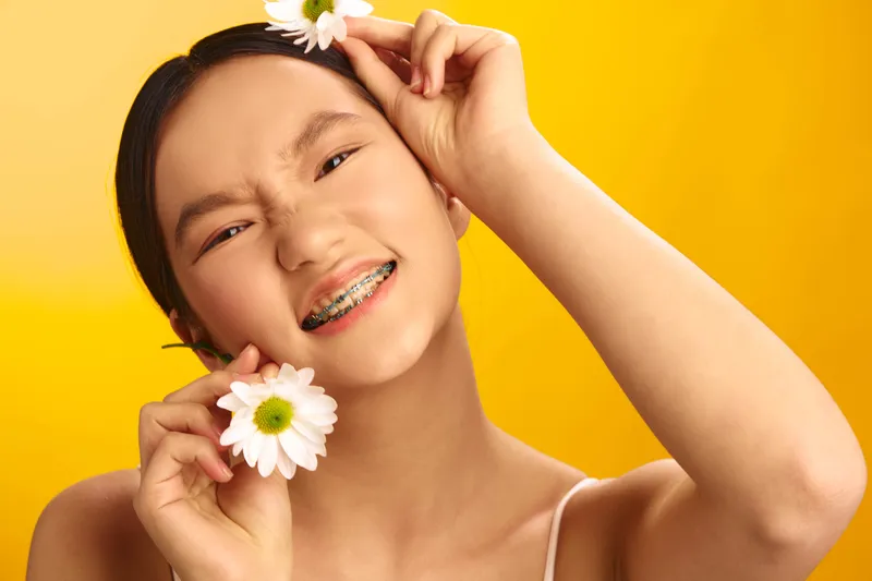 cheerful asian woman smiling with flowers in a bright studio, her carefree pose and sunny backdrop create a vibrant and uplifting mood.