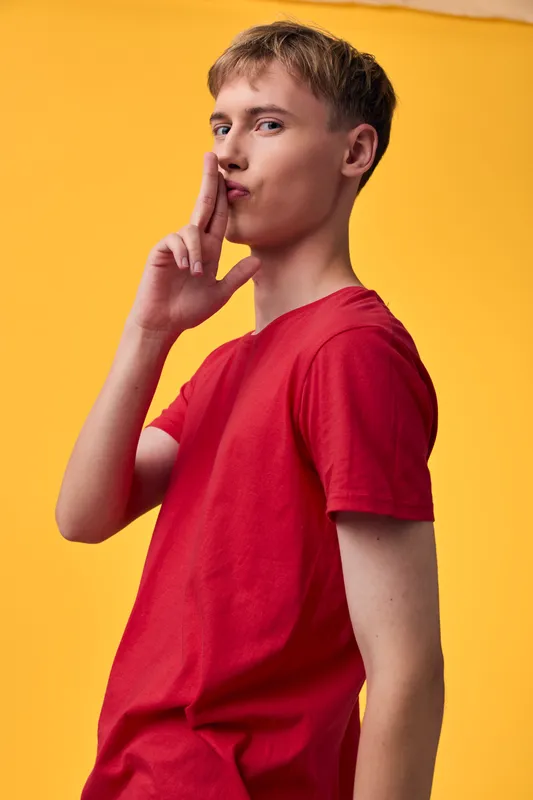 Shushing gesture by a boy in a red shirt against a bright yellow backdrop, conveying secrecy, quiet focus, and a playful hush moment for creative messaging concepts.
