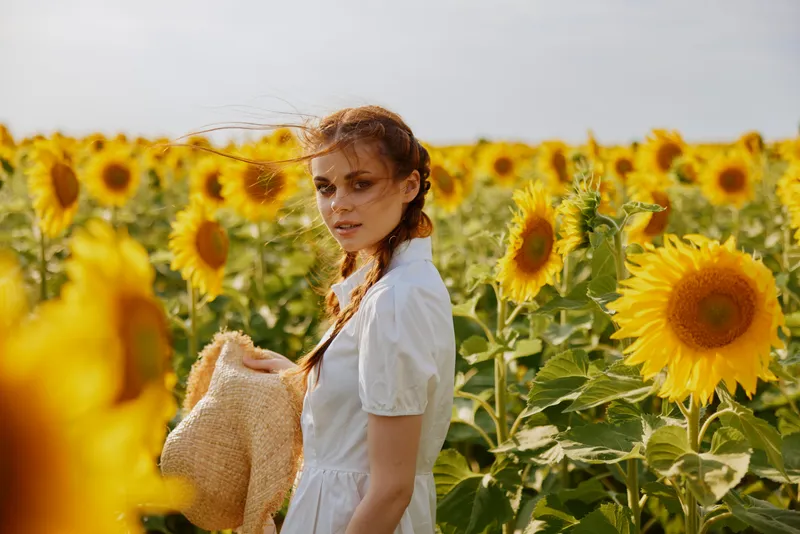 Женщина с двумя косичками в поле с цветущими подсолнухами на фоне пейзажа