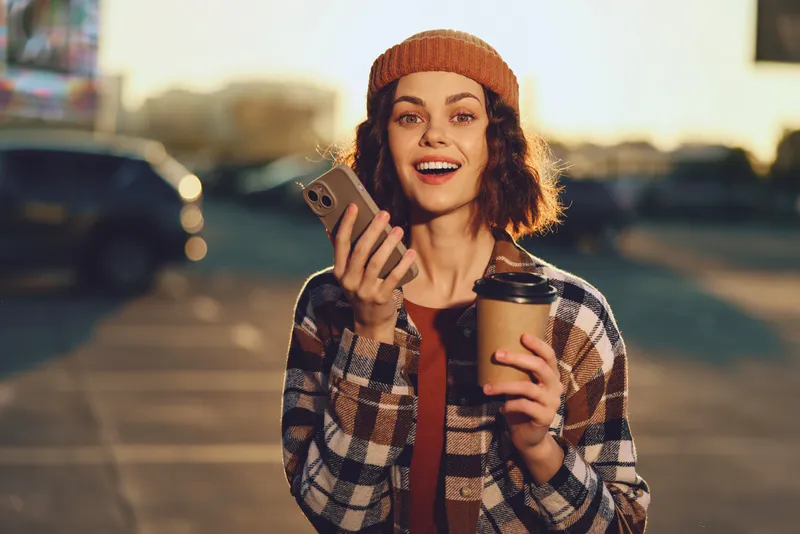 Woman coffee smartphone smile candid urban golden lifestyle moment at golden hour glow, authenticity and mindful living in a relaxed portrait with emotional storytelling and joyful expression.