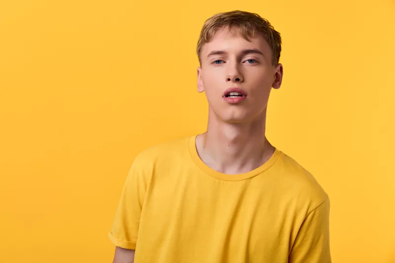 Young man in a yellow tee stands against a vivid yellow backdrop, delivering a bold fashion vibe, casual confidence, and sunny mood ideal for lifestyle and creative stock use