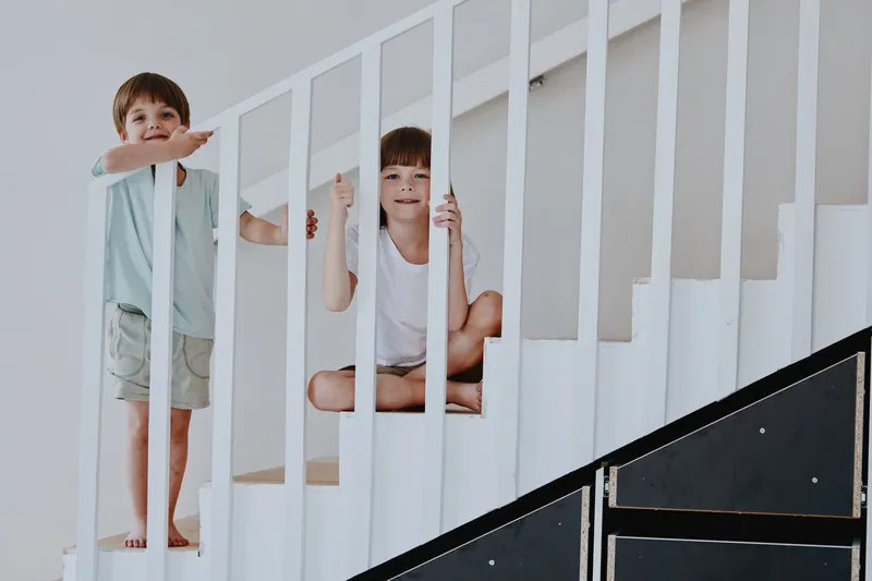 Playful kids enjoying time together on the stairs, capturing moments of joy and laughter in a bright, minimalist home environment.