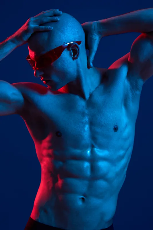 Athletic man with toned muscles poses dramatically against a vibrant backdrop, showcasing strength and confidence in a captivating light. Perfect for fitness themes.