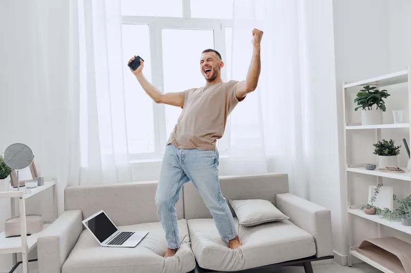 Cheerful man celebrating at home, enjoying digital detox while working remotely, embracing emotional minimalism and life perspective.