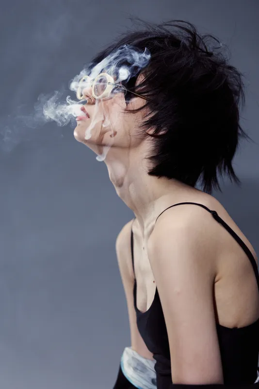 Young woman exhaling smoke in a dark minimalist setting with a moody atmosphere