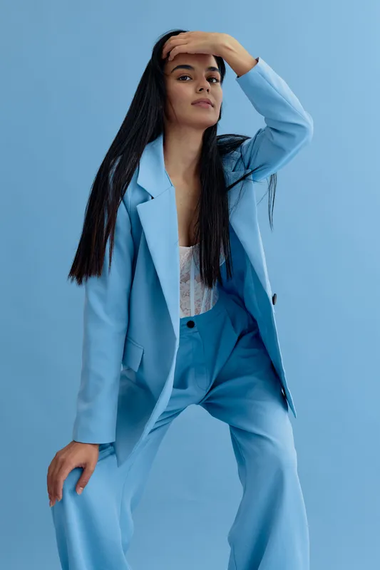 stylish woman with long black hair wearing a light blue suit posing confidently against a matching blue background in a modern fashion portrait