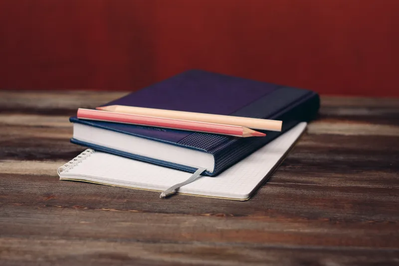 На деревянном столе лежат книга, блокнот, карандаши и офисные документы