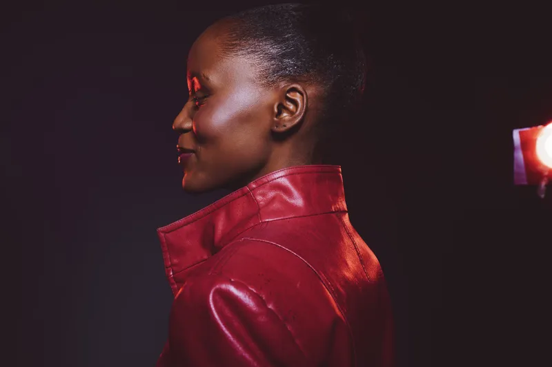 Profile of a dark skinned African woman wearing a red leather jacket, smiling softly against a black background. Concept for fashion, confidence, and beauty with studio lighting.