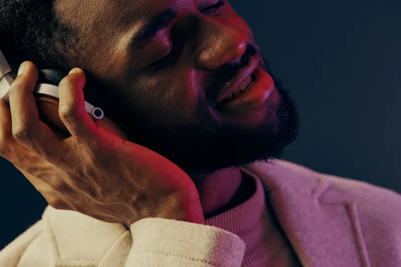Young African man enjoying music with headphones, smiling joyfully in a stylish outfit, vibrant background showcasing emotional connection to sound