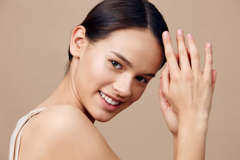 Smiling young woman with clean skin showcasing natural beauty and elegance against a neutral background, perfect for wellness and beauty related content