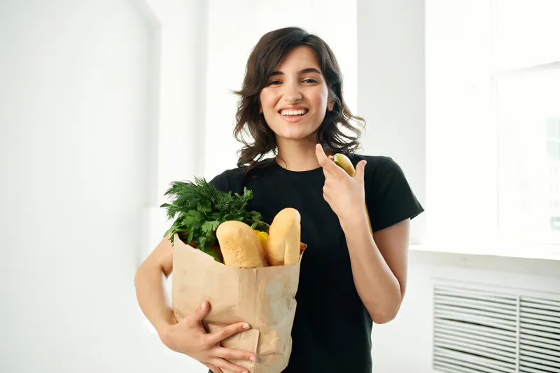 Веселая брюнетка с пакетом продуктов готовит здоровую пищу