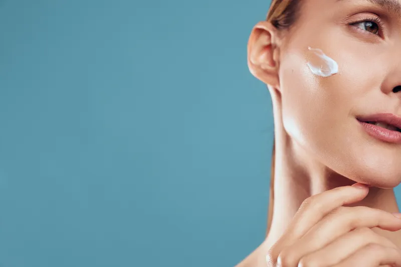 Woman skincare face cream beauty studio blue treatment, close up view, cream on cheek, serene expression, smooth skin texture, soft lighting, self care routine