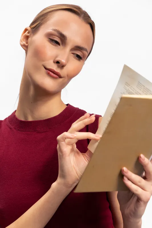 Young woman in red sweater carefully reading a book against white background. Concept of education, knowledge, learning, and focus on study or leisure reading.