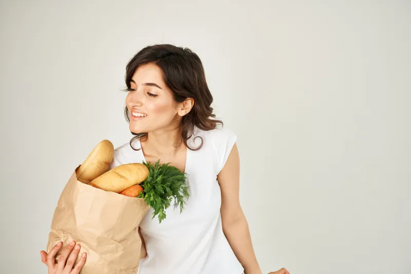 Улыбающаяся женщина с пакетом продуктов в супермаркете на светлом фоне