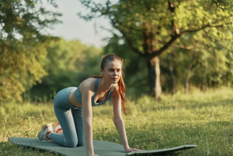 Young athletic woman performing yoga poses in nature, focused on health and fitness, with a serene expression and green surroundings