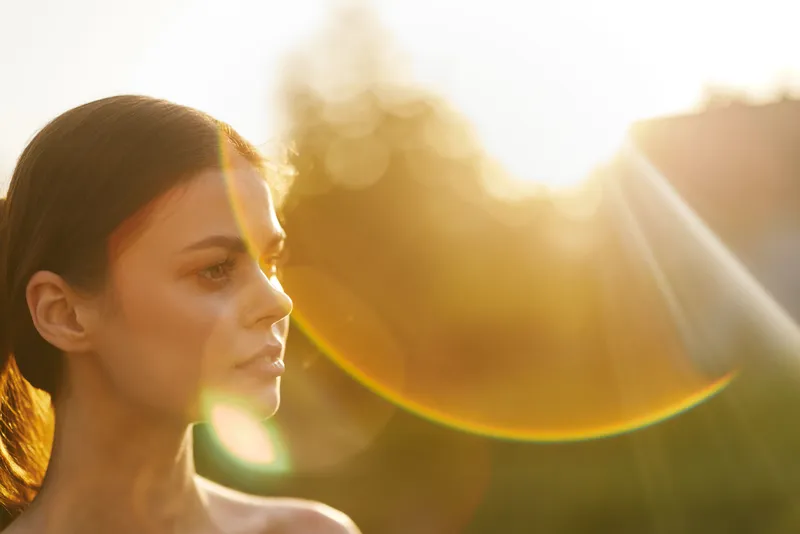 Young woman with long hair in natural sunlight, exuding peace and serenity, against a warm sunset background, highlighting beauty and tranquility