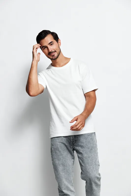 Stylish smiling young man in casual white t-shirt poses confidently against a plain light background, showcasing a relaxed and approachable attitude.