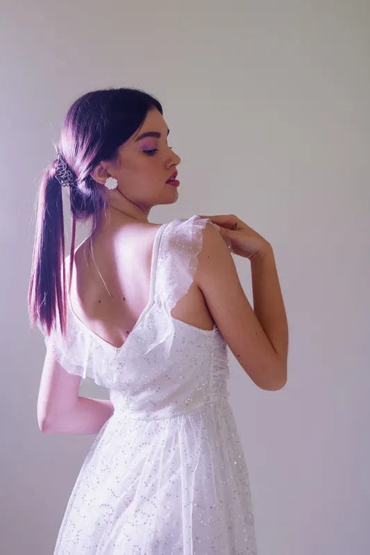 Elegant woman in a white lace dress poses with her back turned, showcasing beauty and fashion in soft studio lighting. Concept for style, elegance, and feminine grace.