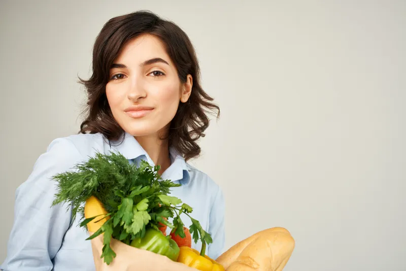 Весёлая женщина с пакетом продуктов из супермаркета покупает овощи