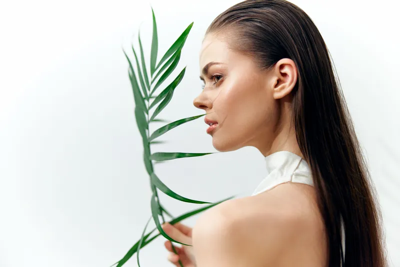 Потрясающая модель с длинными волосами нежно держит зеленый лист, демонстрируя связь с природой