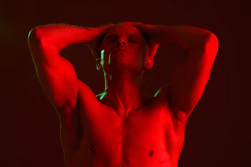 Strong man posing dramatically under bright red lights, showcasing his muscular physique. This striking image captures the essence of power and confidence—black and white.